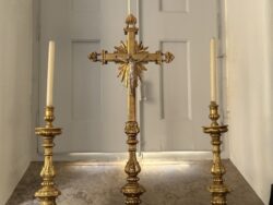 Crucifixo em talha dourada ladeado por castiçais, peça central das celebrações litúrgicas.