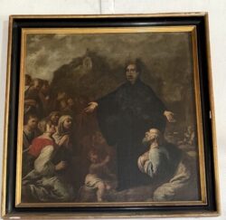 Um missionário, de braços abertos, proclama a fé a uma multidão humilde, sublinhando a dimensão evangelizadora da Igreja.